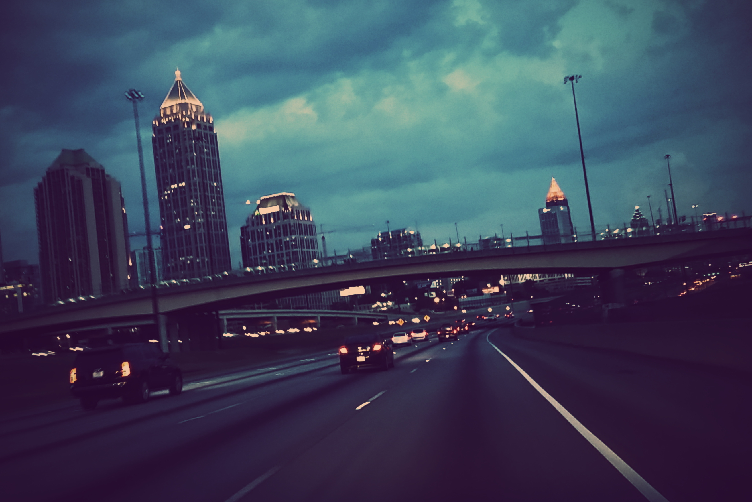 Cars On Highway By Illuminated Modern Buildings Against Cloudy Sky At Dusk