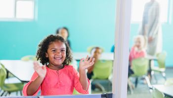 Mixed race girl in preschool smiling, waving