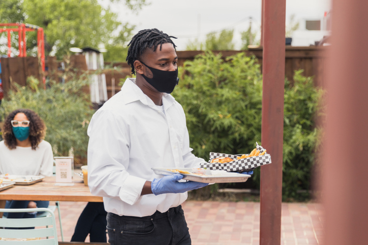 Waiter wears mask and gloves to serve at patio restaurant
