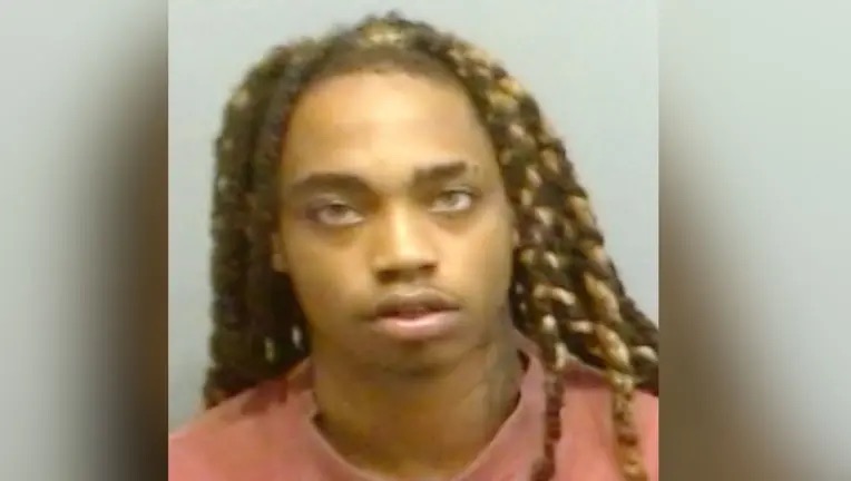 A person with long braided hair wearing a red shirt and looking directly at the camera.