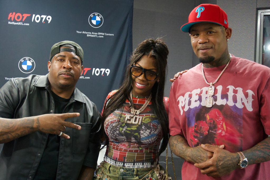 Three people posing in front of Hot 107.9 and BMW Center banners, one wearing a Philadelphia Phillies cap.
